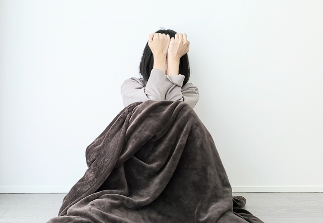 毛布にくるまって座り、顔を隠している女性